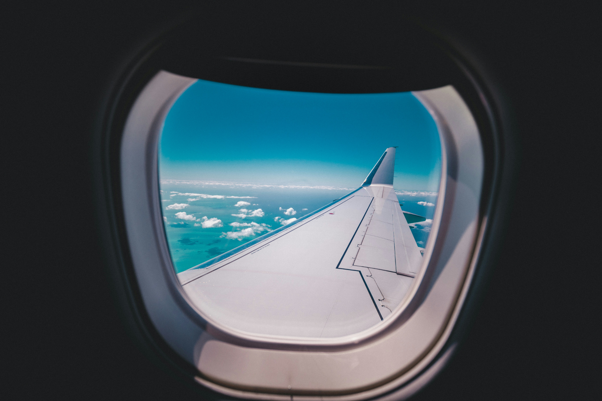 Airplane wing above the turquoise Caribbean seen through a passenger window